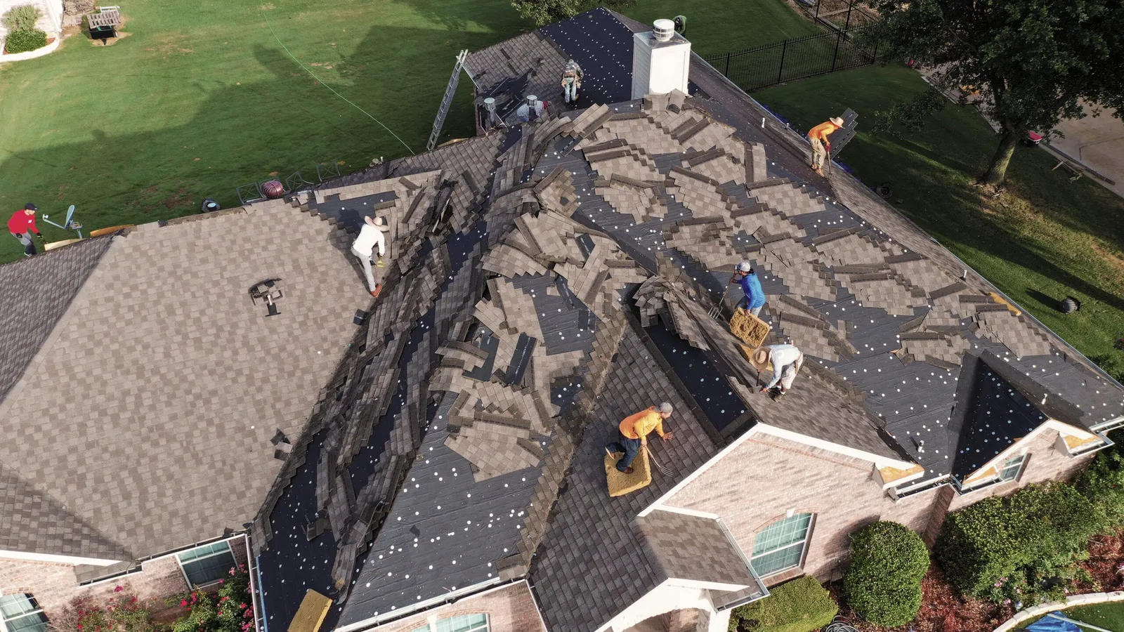 Roofing crew tearing off old shingles down to the decking on a large residential roof